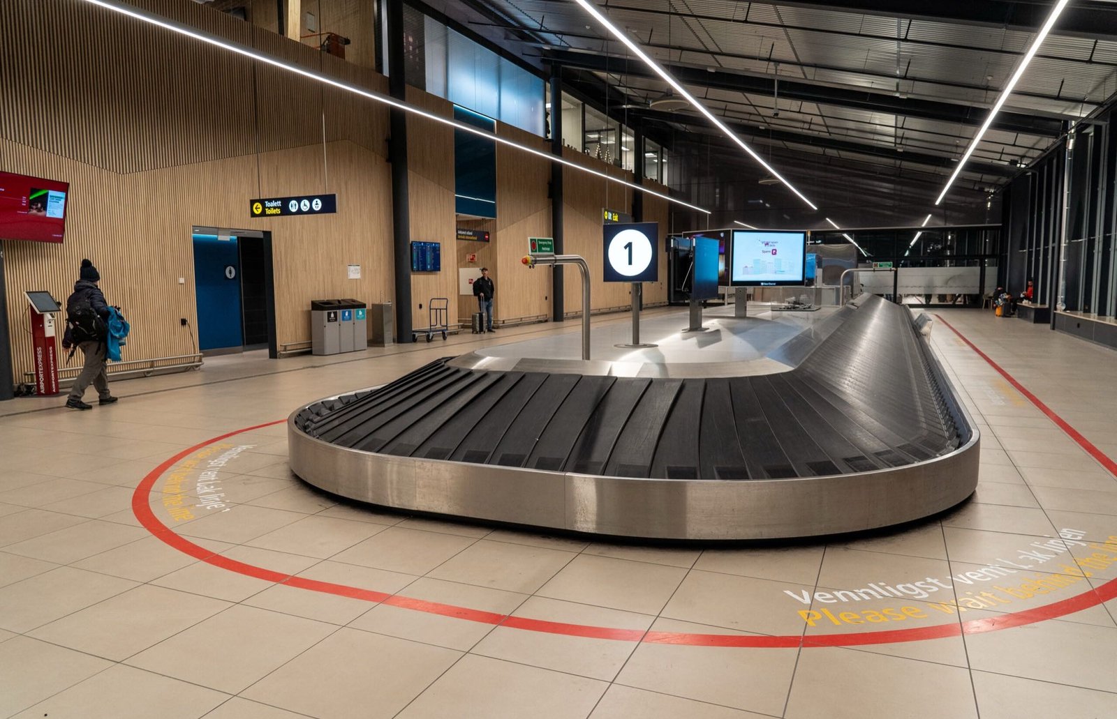 Bagasjebånd i ankomsthallen med teksten «Vennligst vent bak linjen» på gulvet